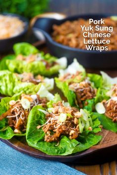 lettuce wraps filled with pork and sauce on a wooden platter next to other dishes