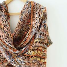 a multicolored crocheted shawl hanging on a wooden hanger against a white wall