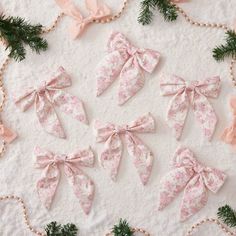 pink bows and pearls are arranged on a white tablecloth with pine branches in the background