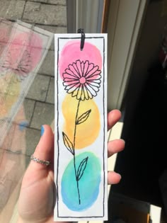 a person holding up a small card with a flower painted on the front and back