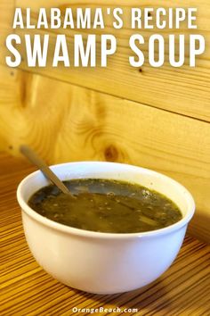 a white bowl filled with green soup on top of a wooden table next to a spoon