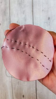 a hand holding a pink piece of fabric with stitching on it