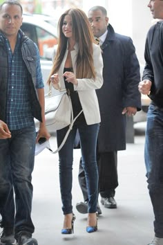 the woman is walking down the street with her hand in her pocket and another man behind her