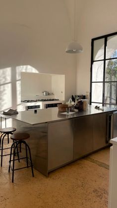 a large kitchen with stainless steel counter tops and stools in front of an open window