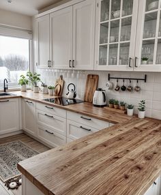 a kitchen with white cabinets and wooden counter tops in front of a large open window