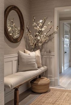 a white bench sitting next to a wall with flowers on it and a round mirror