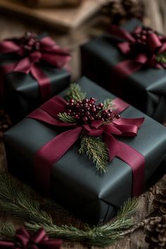 three presents wrapped in black paper and tied with red ribbon, surrounded by pine cones