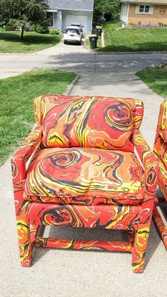 an orange and yellow chair sitting on top of a sidewalk next to a green grass covered yard