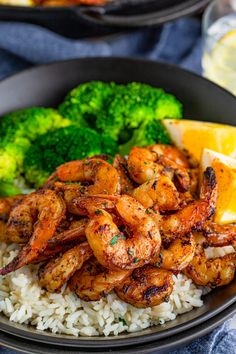 a plate with shrimp, rice and broccoli next to lemon wedges on the side