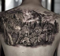 a man's back with wolfs and mountains on his upper half - sleeve