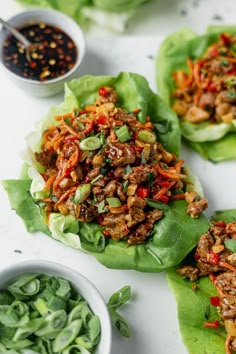 three lettuce wraps filled with meat and veggies next to dipping sauce