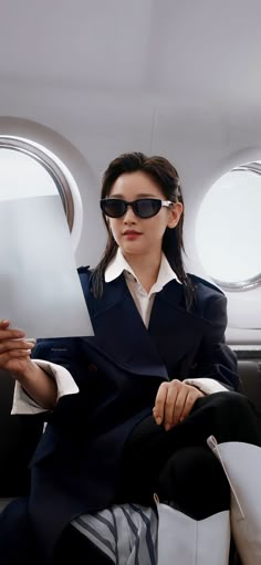 a woman in sunglasses sitting on an airplane reading a piece of paper with her legs crossed