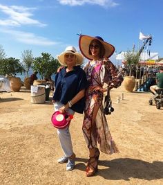 two women standing in the dirt with hats on their heads and one holding a pink frisbee