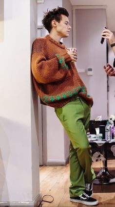 a man leaning against a wall holding a coffee cup