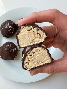 three pieces of chocolate covered ice cream on a white plate with two hands holding them