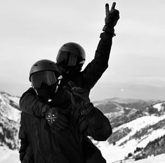 two people standing on top of a snow covered slope with their hands in the air