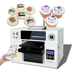 a person holding a remote control in front of a machine with cupcakes on it