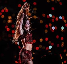 a woman in a red outfit is dancing on stage with her hair blowing in the wind