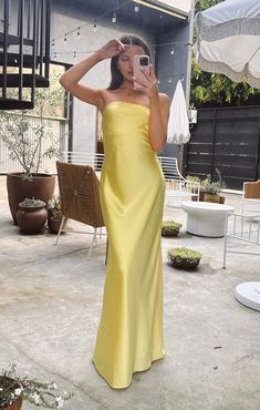 a woman in a yellow dress taking a selfie with her cell phone while standing outside