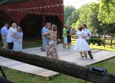 a group of people standing on top of a wooden platform next to a barn building