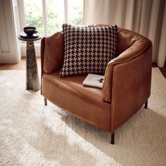 a brown chair sitting on top of a white rug next to a vase and window