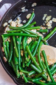 green beans and mushrooms cooking in a skillet with a wooden spoon on the side