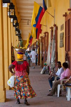 the woman is walking down the sidewalk in front of the storefront with many colorful flags hanging from it's sides