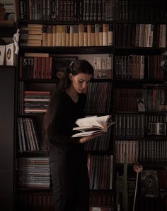 a woman standing in front of a bookshelf holding an open book