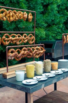 an outdoor table with food and drinks on it, including pretzels hanging over the grill