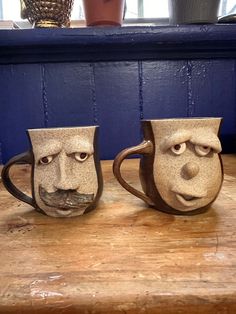 two mugs with faces on them sitting on a table