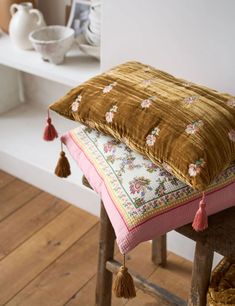 two pillows on top of wooden stools with tassels