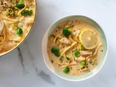 a bowl of soup with broccoli, lemon and noodles on the side next to another bowl