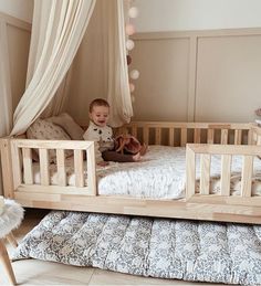 a baby sitting on top of a wooden bed in a room with white drapes