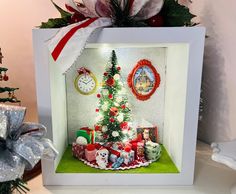 a small christmas tree with presents under it in a shadow box next to a decorated christmas tree