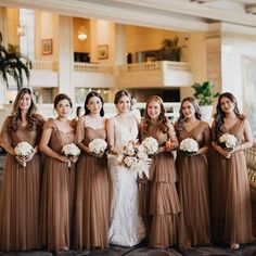 a group of women standing next to each other holding bouquets in front of a building