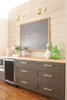 a chalkboard mounted on the wall above an oven in a kitchen with gray cabinets