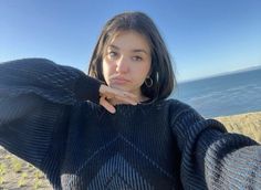 a woman is standing on the beach with her arms behind her head and looking at the camera