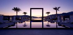 an empty swimming pool surrounded by palm trees at dusk with the sun setting in the background