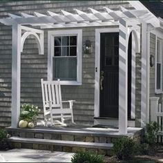 a porch with two rocking chairs and a white trellis on the side of it