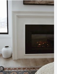 a fire place in a living room next to a window with a painting on the wall