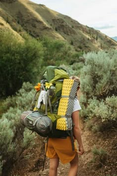 a person with a backpack walking on a trail in the mountains near grass and bushes