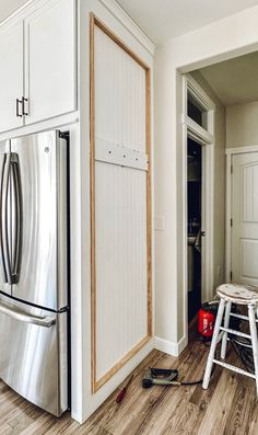 a kitchen with white cabinets and wood floors, including a stainless steel refrigerator freezer