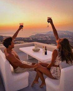 a man and woman sitting on top of a white couch next to each other holding wine glasses