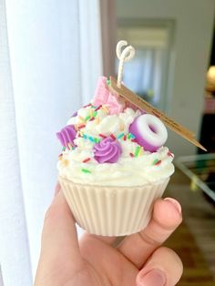 a hand holding a cupcake with white frosting and sprinkles