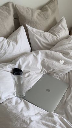 an apple laptop sitting on top of a bed covered in white sheets and pillow cases