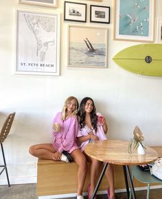 two women sitting at a table in front of pictures and surfboards on the wall