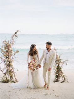 a bride and groom holding hands on the beach