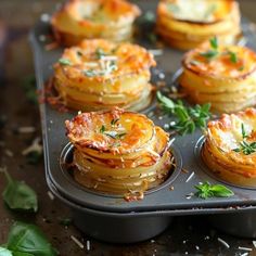 some food is sitting in a muffin tin on a table with herbs and parmesan sprinkles