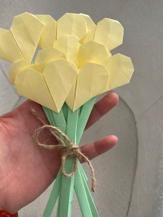 a hand holding a bunch of yellow origami flowers on top of green stems