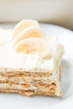 a piece of cake with banana slices on top and frosting, sitting on a white plate